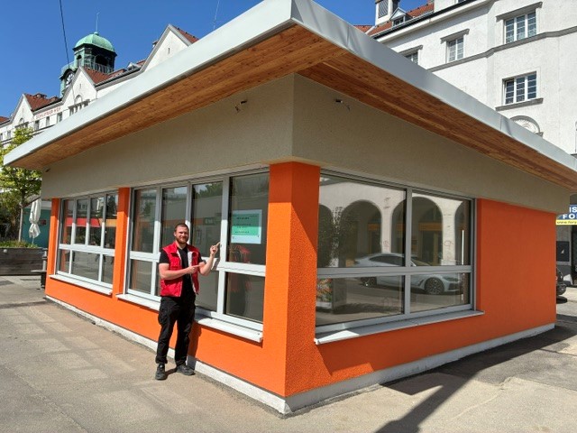 Ein Mann steht vor einem orangenen Marktstand.